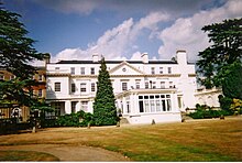 A three-story building in Victorian style set among trees and gardens