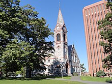 A building with a steeple in the foreground with a brick-clad structure in the brackground