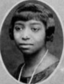 A young Black woman with her hair cut into a short bob with bangs, wearing a strand of pearls or beads, in an oval frame
