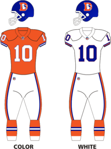 There are two football uniforms. The one on the left has an orange shirt with a white ten, the one on the right a white shirt with a blue ten. Both have blue helmets with an orange D, a horse inside it and white trousers with orange and blue stripes.