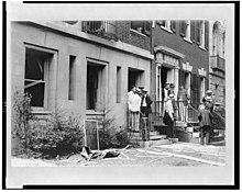 Black and white photo of people in front of a damaged house
