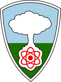 A shield with a white mushroom cloud rising from a red atom against a blue sky