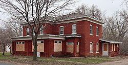 A two-story brick house with irregular one-story projections and boarded-up windows