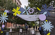 Rectangular scaffolding creating an entrance to the XOXO venue. Blue, yellow, and purple cutouts form flowers and circular shapes, forming the letters "XOXO"