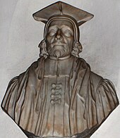 A stone bust of a man (head and shoulders), with beard, cap and robes