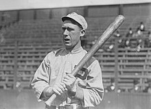 A black-and-white photograph of a man wearing a baseball sweater with a "P" over the left breast and a crownless baseball cap holding a baseball bat over his left shoulder