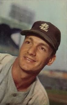 A man in a gray baseball uniform wears a dark cap with an overlapping "STL" on the center
