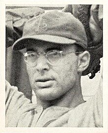 A man wearing glasses and a dark baseball cap with an overlapping "STL" on the front has his hands behind his head as if preparing to throw a ball.