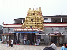 A gray temple with red and white banded frieze and a gilded multi-tier entrance.