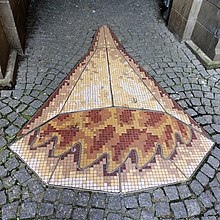 On Peter Street in Dundee, there is a mosaic on the ground commemorating Grisell Jaffray, the last woman to be burnt as a witch there. There are two elements to the mosaic, one representing fire and the other representing water. This image is of gold and red mosaic tiles representing fire, surrounded by cobble stones.