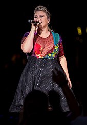 A blonde woman holding a microphone and wearing a dress.