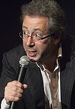 A man in a suit and wearing glasses talking into a microphone