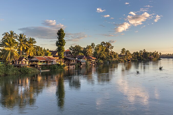 金色时刻眺望湄公河畔的高脚屋、树木和云彩。摄于老挝四千岛地区东德岛和东阔岛之间的桥上。
