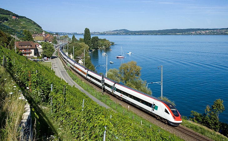 图为在侏罗山脚铁路（英语：Jura foot railway line）上运行的两列瑞士联邦铁路ICN摆式列车（英语：SBB-CFF-FFS RABDe 500），列车背后是比尔湖。