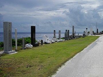 various cenotaphs on grass lined up from lower left to mid right side with ocean in background.