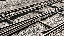 Three rails cross the picture from left to right supported on thick timbers; occasional smaller timbers cross between these and stone chippings fill the space between them.