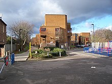 A footpath stretches in a straight line into the distance, next to a large yellow rectangular building.