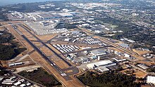 Aerial view of an airport with several runways and taxiways, surrounded by warehouses and other buildings.