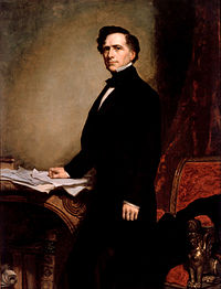 Franklin Pierce, a man with brown hair and a blacks suit, stands with his right hand resting upon papers on a table.