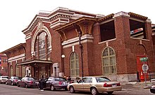 A red-brick train station, with cars in front