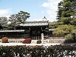 Structure with pointy roof behind a wooden fence and gate.