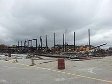 A few standing, charred support beams surrounded by the ashes and remains of the burnt structure