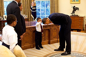 US President Barack Obama bends down to allow the son of a White House staff member to touch his head