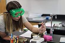 A CFHS student in goggles mixes an amalgum in chemistry class