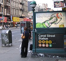 One of the station's entrances as seen in 2005. On the right, there is an advertisement above a sign with the words "Canal Street Station" and the emblems of the routes that stopped there. To the left of the sign, at the center of the image, is a pole with a green globe. The sidewalk and street are to the left.