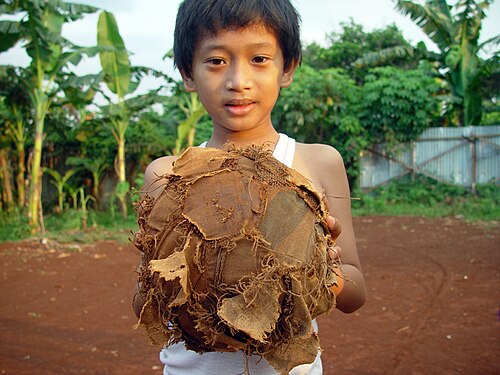 A young boy, in Jakarta Indonesia, holds a tattered football (soccer ball).