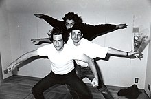 Black-and-white photo of three men posing lined up in crouched positions with their arms outstretched