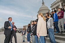 Two older white men in suits address a group of teenagers assembled the the steps of the U.S. Capitol.