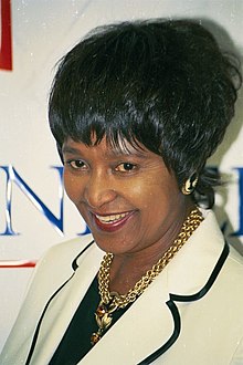 a middle-aged black woman wearing bobbed hair, a white blazer, and a gold necklace.