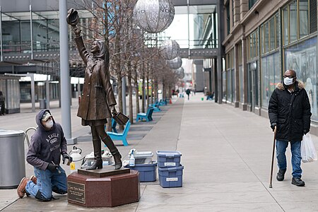 A worker cleans the Mary Tyler Moore statue as a man walks by in a medical face mask in Minneapolis, Minnesota