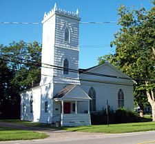 A white building with gentle pointed roof, pointed-arch front windows and a tall square tower on the front with a jagged top