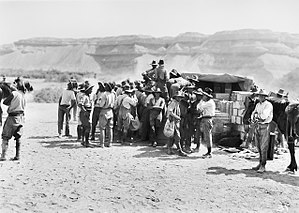 Soldiers gathered round stacks of crates partly covered with a tarpaulin where food is being sold