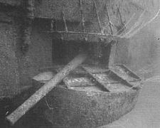 Underwater photograph of a gun protruding from an opening in the side of a sunken ship.