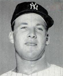 A man in a light baseball jersey and dark cap