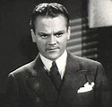 Head and shoulders shot of Cagney, looking stern, wearing a suit with a white handkerchief in his pocket.