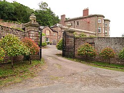 A red-brick, three-storey, historic house with a red-brick wall and gates in front