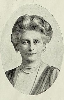 older white woman with bouffant gray hair, wearing pearls or beads.