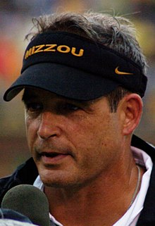 Head shot of Gary Pinkel wearing a visor talking in a microphone.