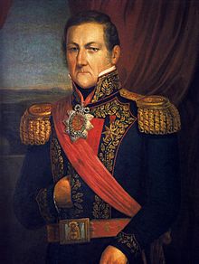 Half-length painted portrait of a man with curly hair, long sideburns and blue eyes who wears a heavily embroidered military tunic with high collar, gold braid epaulettes and a red sash of office