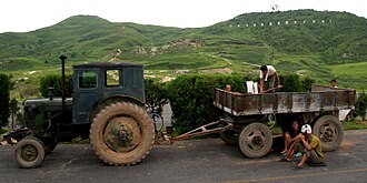 农民在拖拉机的拖车前休息。背景上有小山。