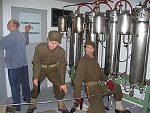 Two saboteurs and a facility employee shown adjacent to the electrolysis chambers