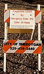 A sign upon a traffic barricade in front of a playground in Sheboygan notifies the public that the equipment is closed due to Evers's stay-at-home order, and of the consequences for violating it.