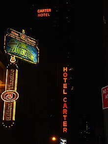 Nighttime view of the Hotel Carter. There are four illuminated signs in the picture: two signs reading "Hotel Carter" to the right, and two signs for the Hilton Theatre (now the Lyric Theatre) to the left.