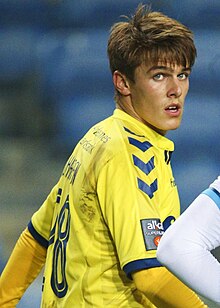 A man wearing a yellow and blue football jersey looks back at the camera.