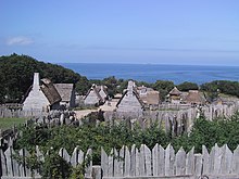 A color picture of the reconstructed Plymouth Plantation in Plymouth. All upright wood logs are faded pale from the sun.