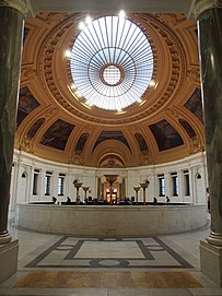 View of the domed rotunda, which contains a skylight at the center, surrounded by murals on the ceiling. The rotunda connects the lobby with the exhibition galleries of the Heye Center.